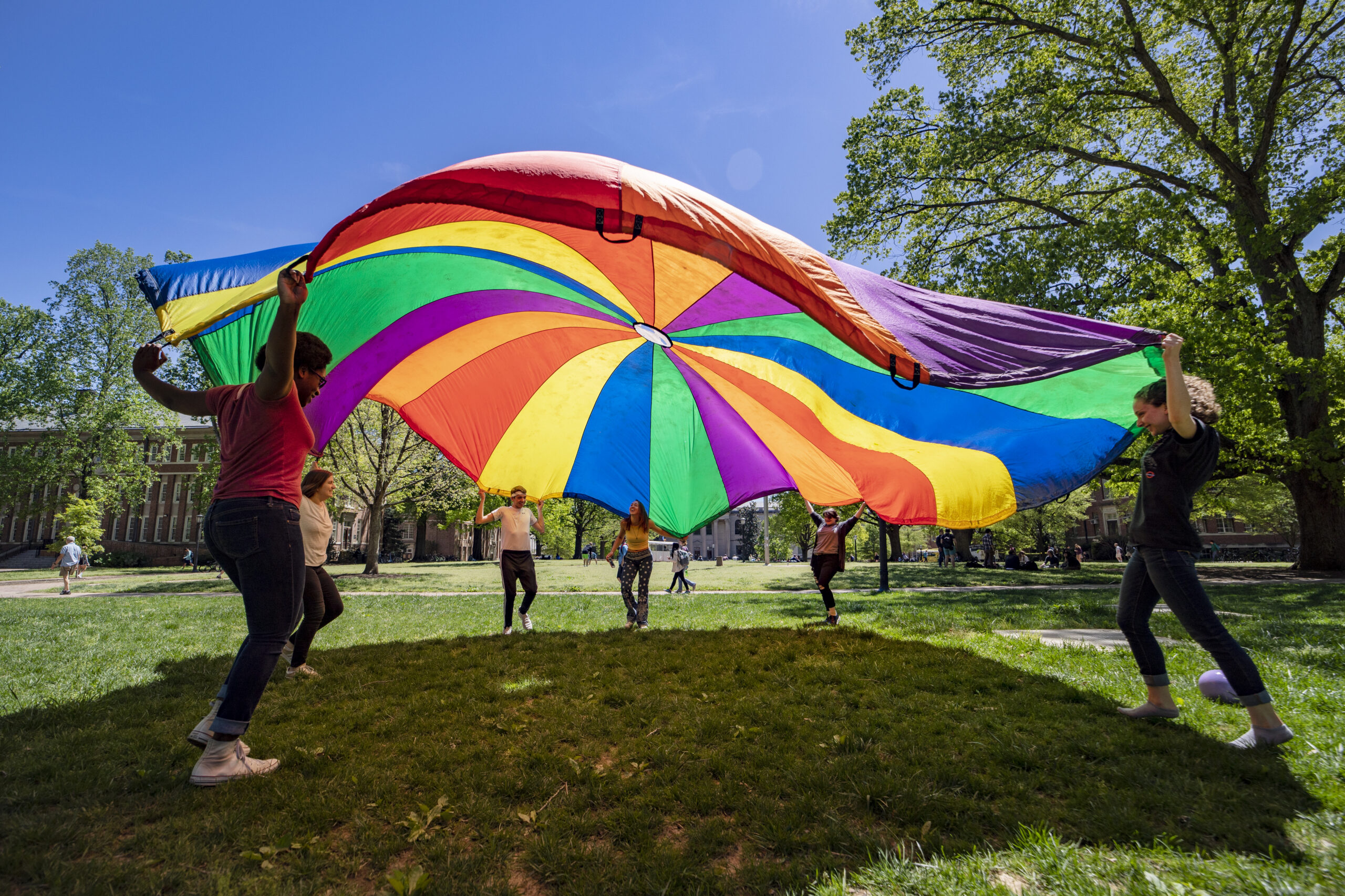 A group of students flap a large rainbow parachute on Polk Place at UNC.
