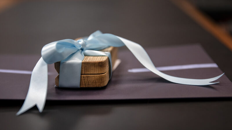 A wooden gift gift with a Carolina blue ribbon sits on a table.