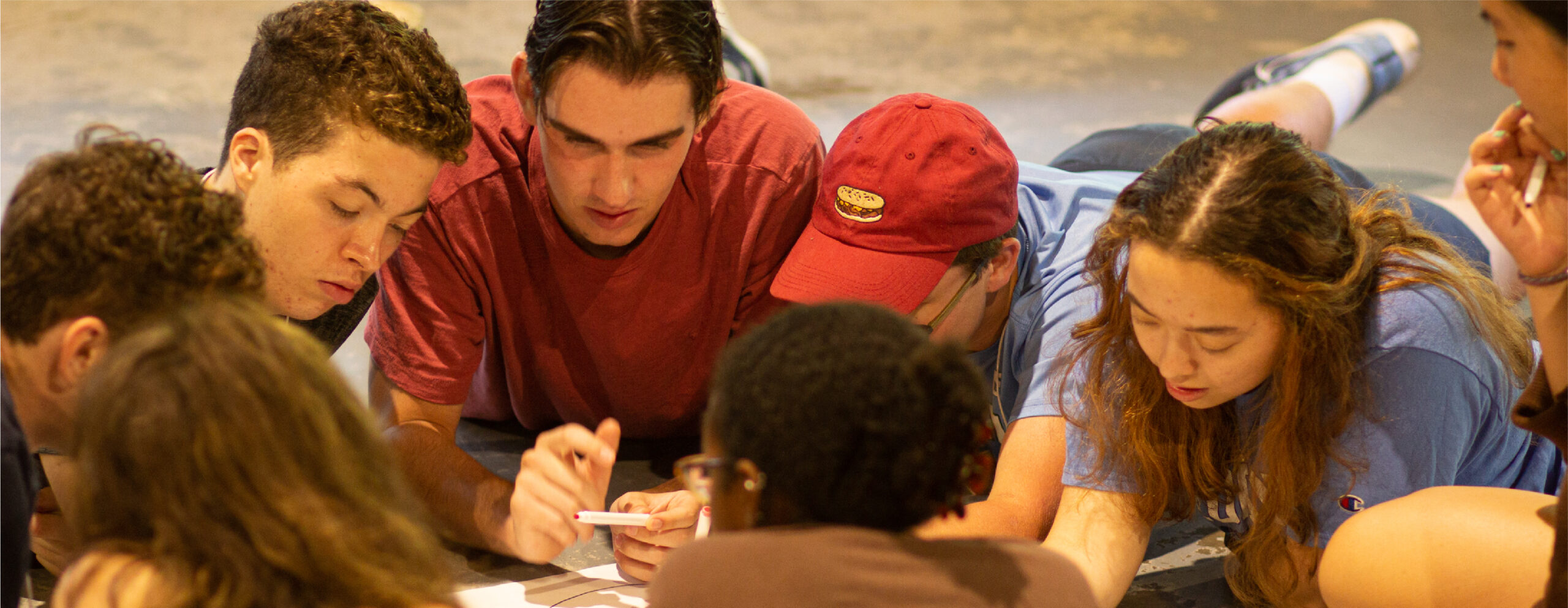 Students lying on the ground writing together on a large sheet of paper during a group activity at an NC Fellows retreat.