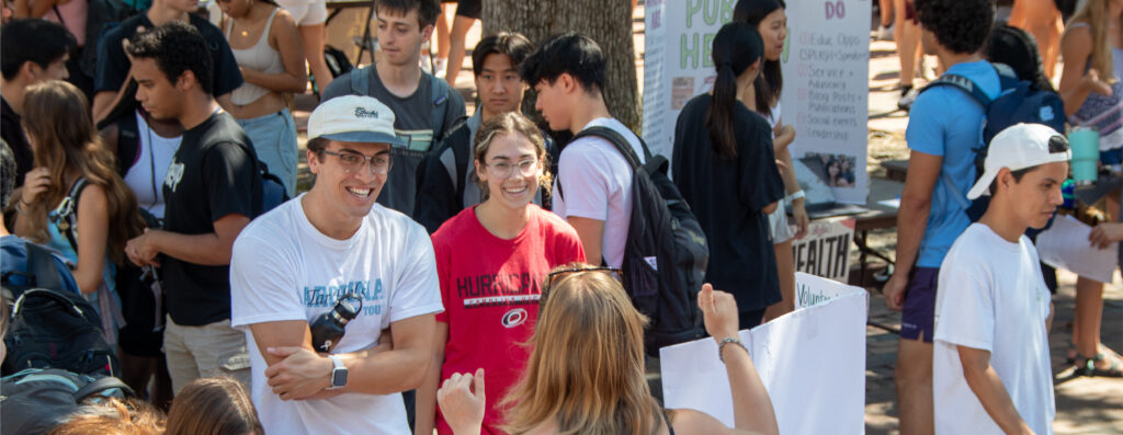 Smiling students learning about a student organization in a packed Pit at SmallFest 2023.