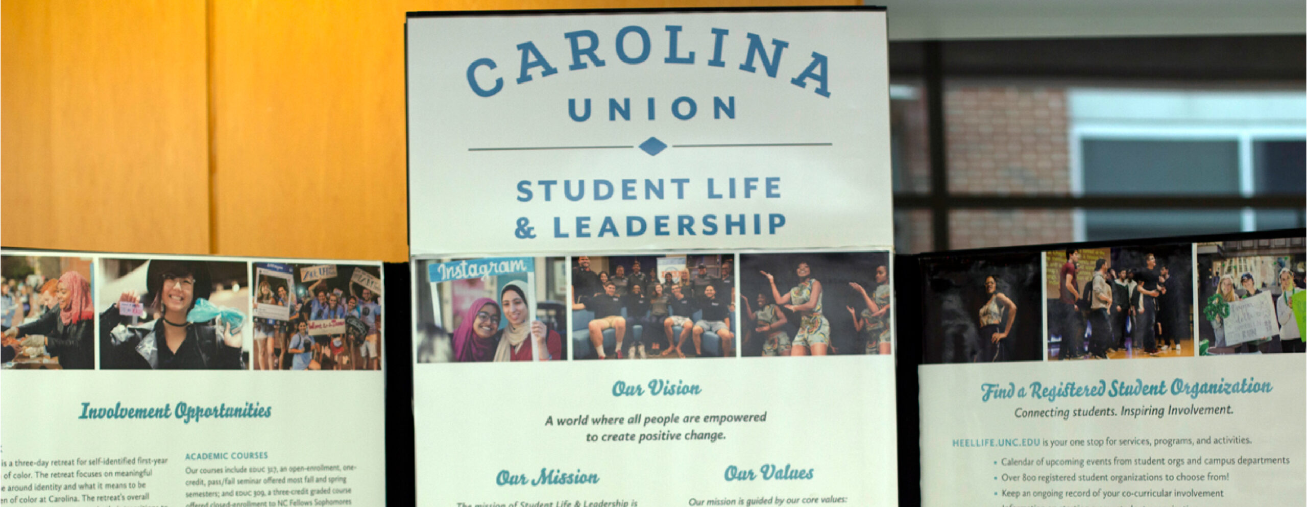 A folding poster display with the Carolina Union and SLL logos displaying photos of students and listing the Mission and Vision of Student Life & Leadership as a department.