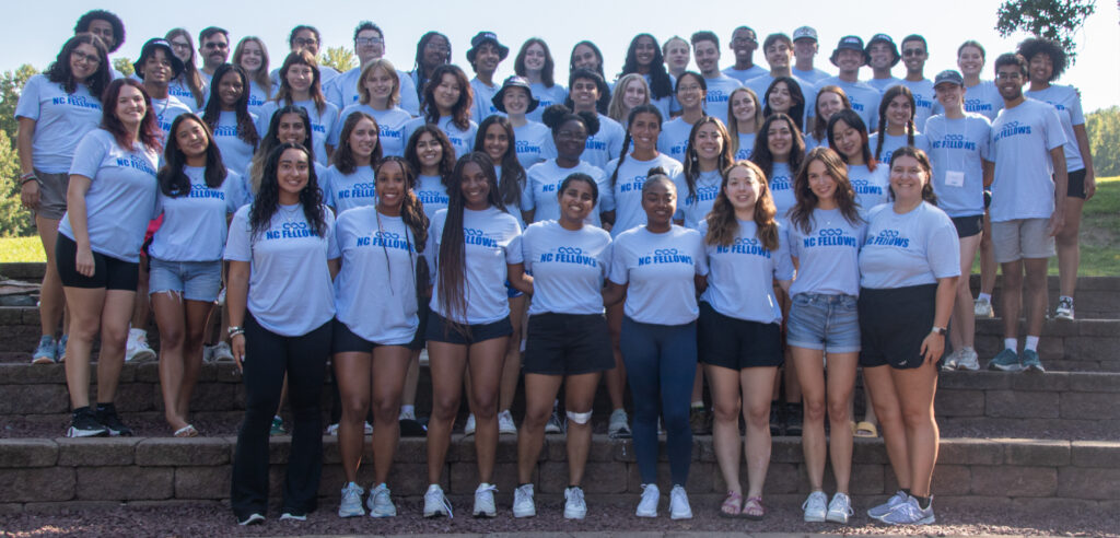 Group photo from the NC Fellows 2024 retreat, featuring members posing in their light blue NC Fellows shirts standing on stairs outdoors.