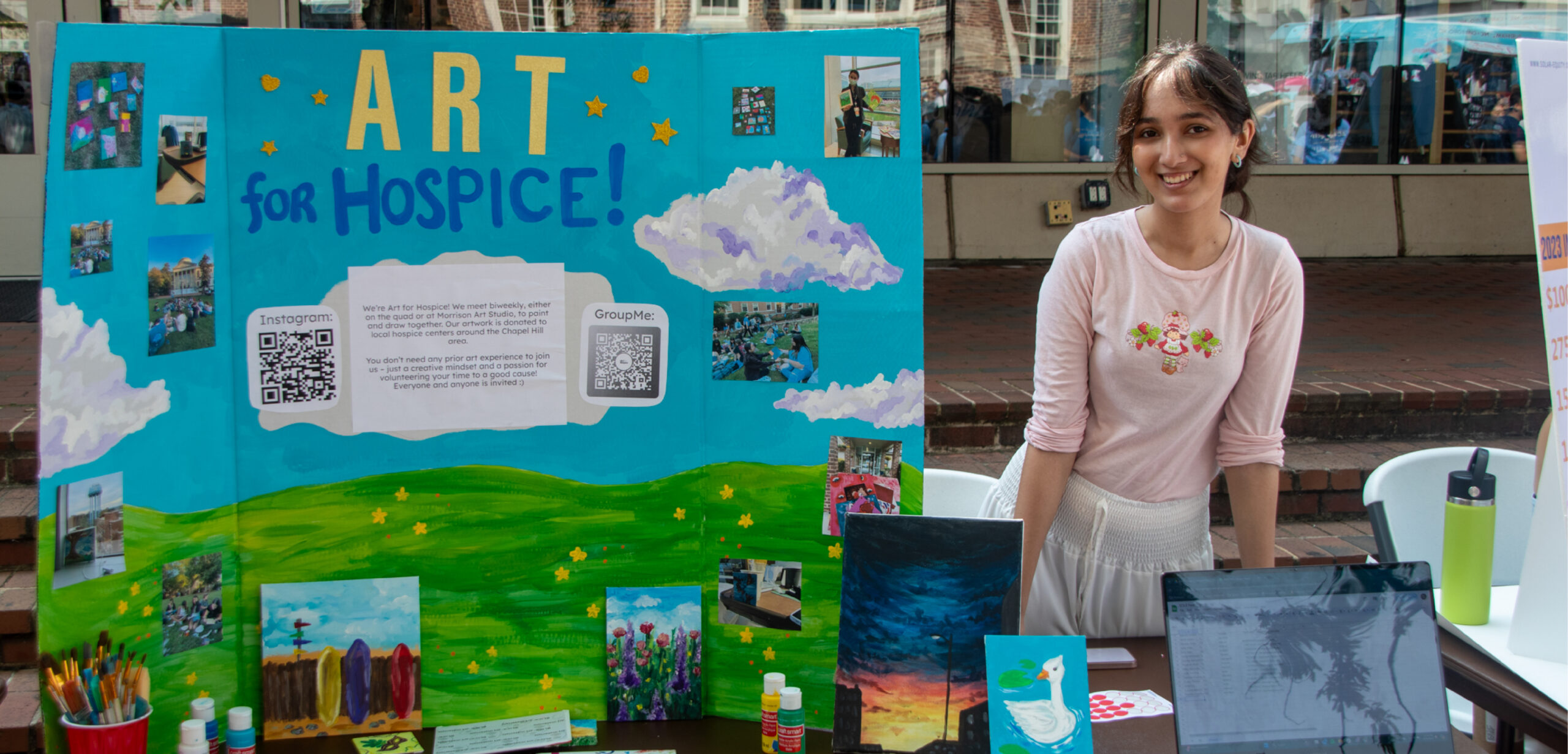 A student poses with a painted poster board for the Art for Hospice student org at S.O.L.E. Fest.