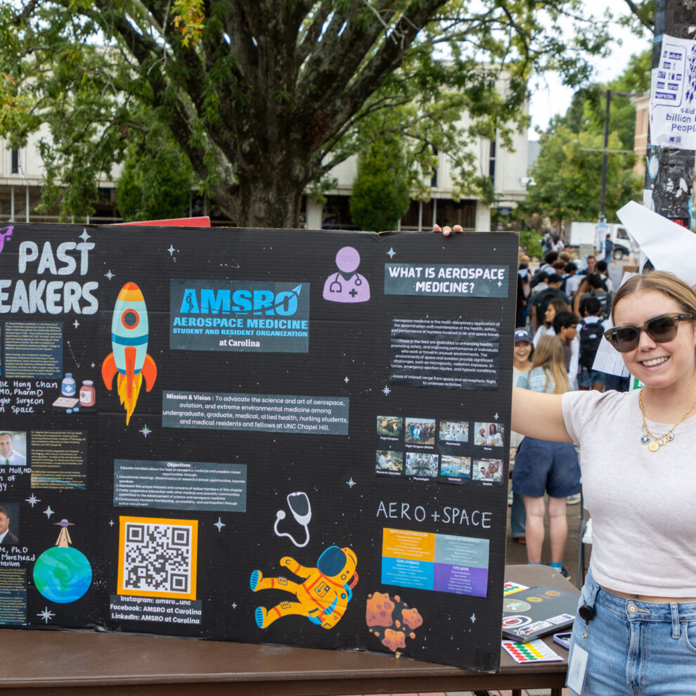 A student wearing sunglasses poses with her poster outside the pit at SOLE Fest 2025.